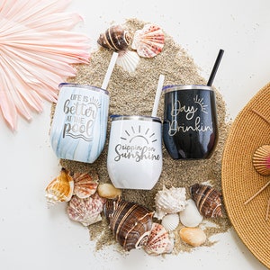 K&ouml;nnte beinhalten: Drei Edelstahlbecher mit sommerlichen Spr&uuml;chen. Die Becher stehen auf einem Sandbett mit Muscheln und einem Strohhut. Die Becher sagen "Life is better at the pool", "Sipping on Sunshine" und "Day Drinkin".