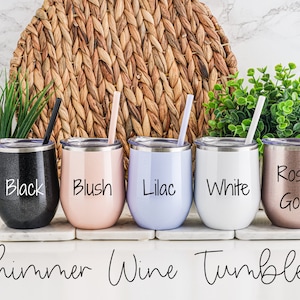 K&ouml;nnte beinhalten: F&uuml;nf schimmernde Weintumbler in verschiedenen Farben: Schwarz, Blush, Lila, Wei&szlig; und Ros&eacute;gold. Jeder Tumbler hat einen passenden Strohhalm und einen Deckel. Die Tumbler sind in einer Reihe auf einer wei&szlig;en Oberfl&auml;che angeordnet. Der Text "Shimmer Wine Tumblers" steht unter den Tumblern.