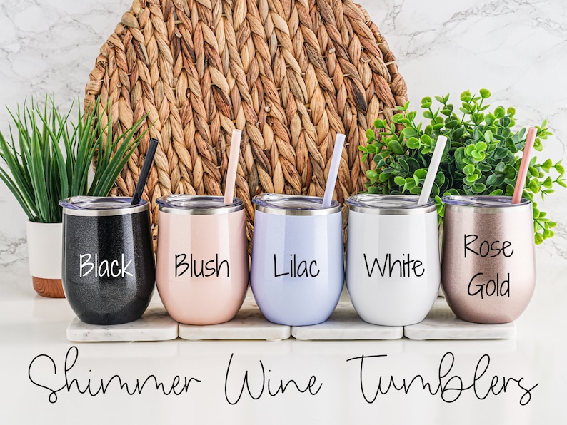 K&ouml;nnte beinhalten: F&uuml;nf schimmernde Weintumbler in verschiedenen Farben: Schwarz, Blush, Lila, Wei&szlig; und Ros&eacute;gold. Jeder Tumbler hat einen passenden Strohhalm und einen Deckel. Die Tumbler sind in einer Reihe auf einer wei&szlig;en Oberfl&auml;che angeordnet. Der Text "Shimmer Wine Tumblers" steht unter den Tumblern.