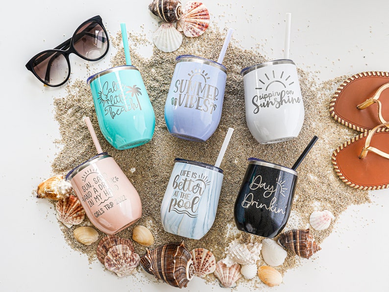 K&ouml;nnte beinhalten: Sechs Edelstahlbecher mit verschiedenen Sommermotiven und Spr&uuml;chen. Die Becher sind von Muscheln und Sand umgeben. Die Spr&uuml;che lauten: "Sun, Sand, and a Drink in my Hand", "Life is Better at the Pool", "Day Drinkin", "Sippin on Sunshine", "Summer Vibes" und "Salt, Little Beach".