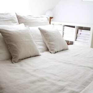 May include: A white linen bed with a white duvet cover and several white pillows. The bed is made with crisp, clean linens and is ready for a good night's sleep.