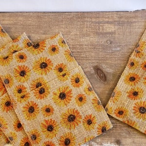 May include: Set of eight burlap napkin rings with a sunflower print. The rings are brown with yellow and orange sunflowers.