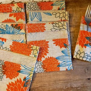 May include: A set of 10 burlap place card holders with a floral design in shades of orange, blue, and white. The holders are folded and have a pocket for a place card.