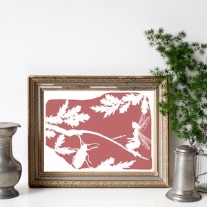 May include: A framed print with a pink background and white silhouettes of a fairy, a beetle, and leaves. The frame is gold with a decorative border.