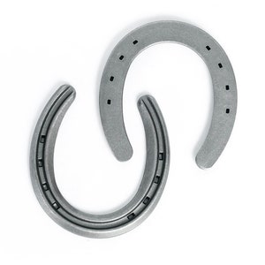 May include: Two silver-colored horseshoes arranged in a decorative pattern against a white background. Each horseshoe has a U-shape with multiple nail holes. The metal has a slightly textured appearance.