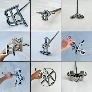May include: Nine different metal branding irons with wooden handles. The branding irons are shaped like letters and symbols, including a "B", "P", "M", "V", "R", "S", "J", and a combination of "B" and "J".