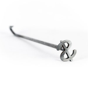 May include: A silver metal branding iron shaped like a dollar sign with a long handle.