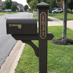 May include: A dark brown mailbox and post with a gold-colored address plate displaying the number 1031. The mailbox has a gold-colored handle and is mounted on a wooden post with decorative brackets. The scene is set in a suburban neighborhood.
