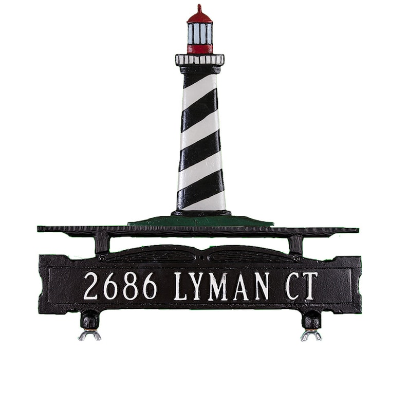 May include: Black metal mailbox with a lighthouse design. The mailbox has a black and white striped lighthouse with a red roof and a green base. The mailbox also has a black metal sign that says "2686 LYMAN CT".