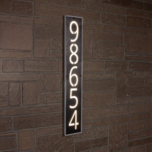 May include: A black metal house number plaque with white illuminated numbers. The numbers are 98654.