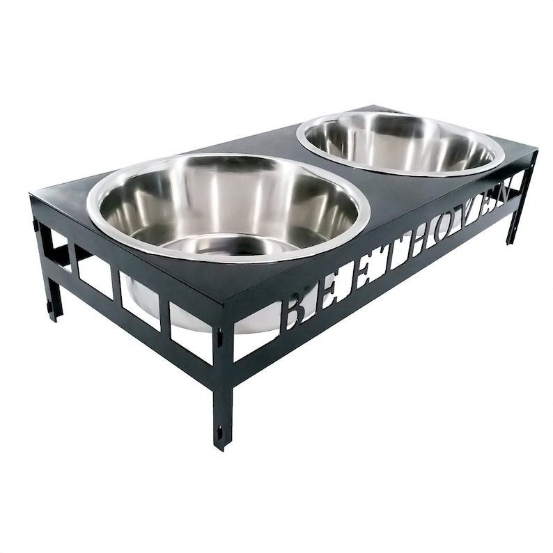 May include: Black metal dog bowl stand with two stainless steel bowls. The stand has the word "BEETHOVEN" cut out in the front.