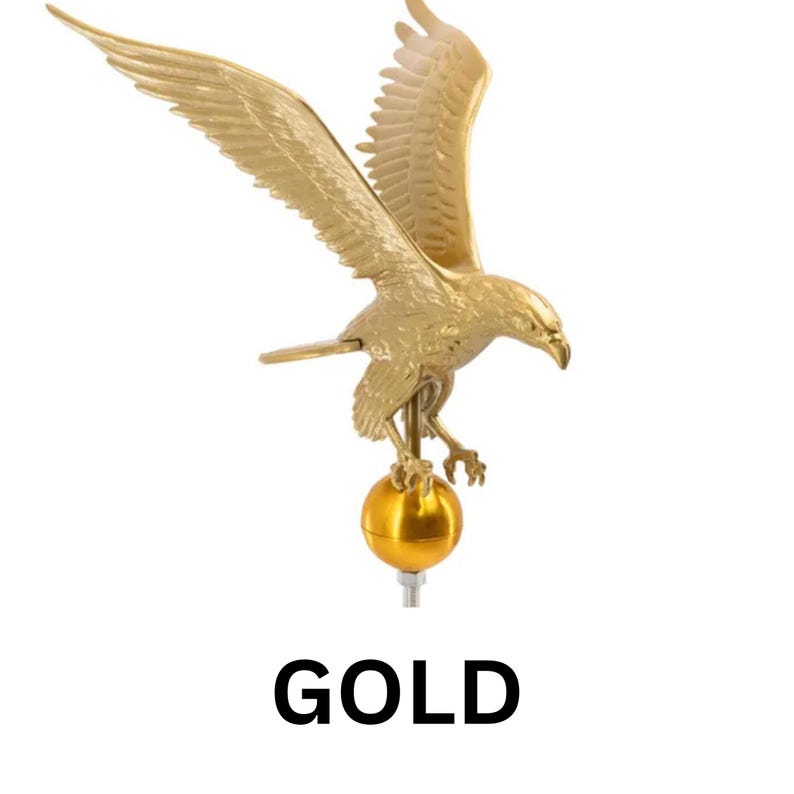 May include: A gold-colored metal eagle figurine with wings spread wide, perched atop a smooth, spherical gold ball. The eagle is depicted in a downward-facing flight position with detailed feathers and talons. The word GOLD is printed below.