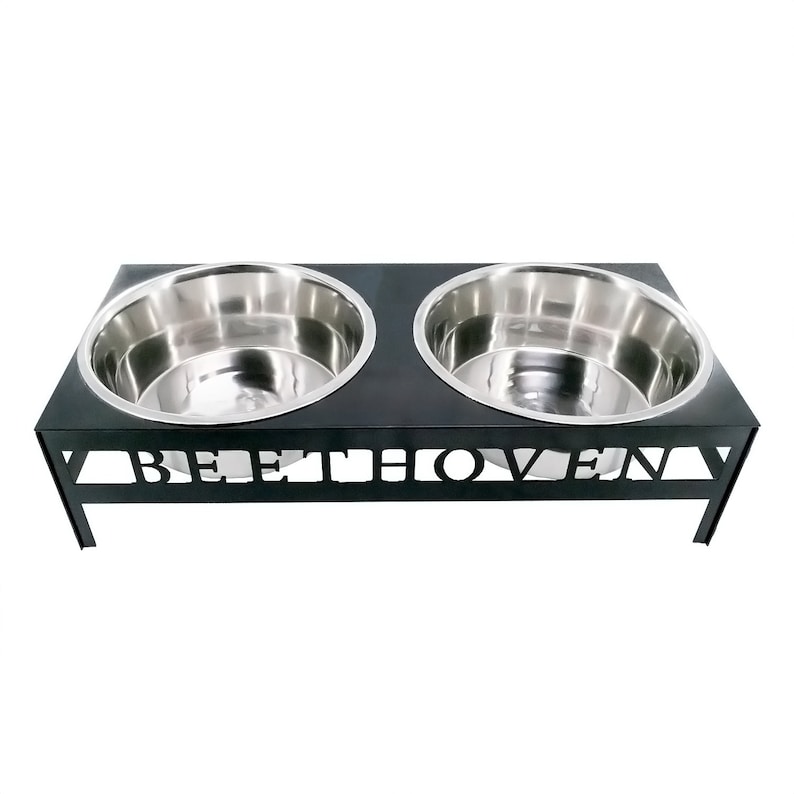 May include: Black metal double dog bowl stand with the word "Beethoven" cut out in the front. The stand has two stainless steel bowls.