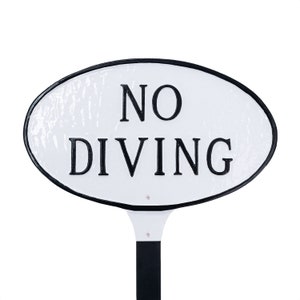 May include: White oval sign with black border and text that reads "NO DIVING" on a black metal post.