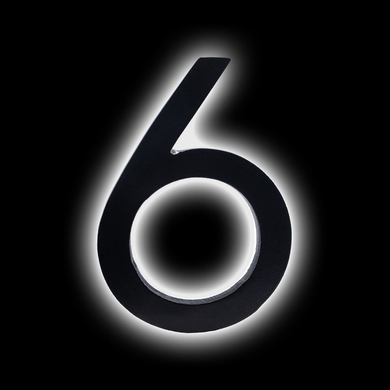 May include: Black metal house number six with a white outline. The number is on a black background.