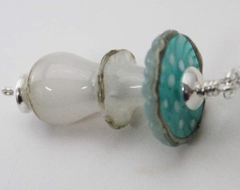 May include: A silver chain necklace with a white glass pendant and a turquoise blue and white glass bead. The bead has a white polka dot pattern.