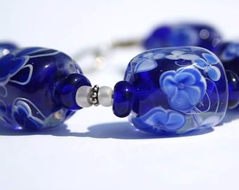 Könnte beinhalten: Nahaufnahme einer blauen Glasperlenkette mit weißen Blumenmustern. Die Perlen sind rund und haben eine glänzende Oberfläche.