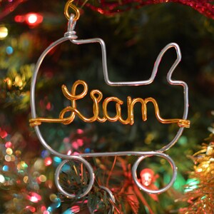 May include: A silver wire ornament shaped like a baby carriage with the name Liam spelled out in gold wire.