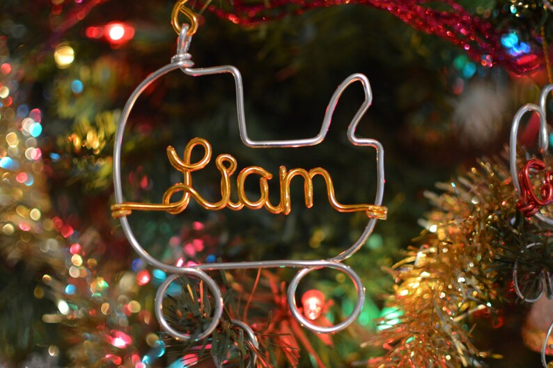 May include: A silver wire ornament shaped like a baby carriage with the name Liam spelled out in gold wire.