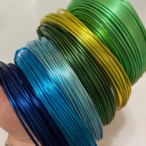 May include: A stack of colorful metallic wire spools in shades of green, yellow, blue, and navy. The wire is perfect for crafting and jewelry making.