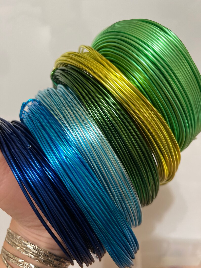 May include: A stack of colorful metallic wire spools in shades of green, yellow, blue, and navy. The wire is perfect for crafting and jewelry making.