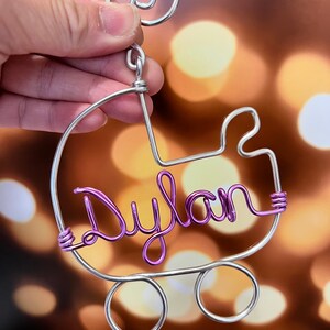 May include: A silver wire baby carriage ornament with the name "Dylan" spelled out in purple wire.