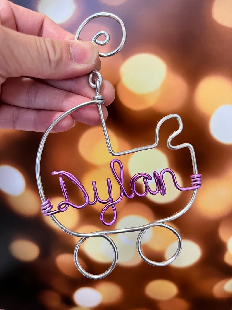 May include: A silver wire baby carriage ornament with the name "Dylan" spelled out in purple wire.