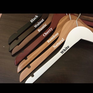 May include: A set of wooden hangers in various colors, including black, walnut, rustic, cherry, bamboo, natural, and white. The hangers are all made of wood and have a smooth finish.