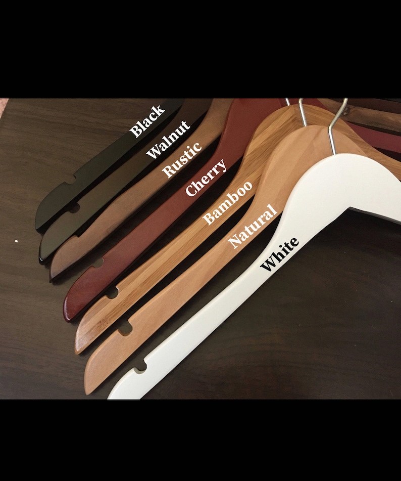 May include: A set of wooden hangers in various colors, including black, walnut, rustic, cherry, bamboo, natural, and white. The hangers are all made of wood and have a smooth finish.