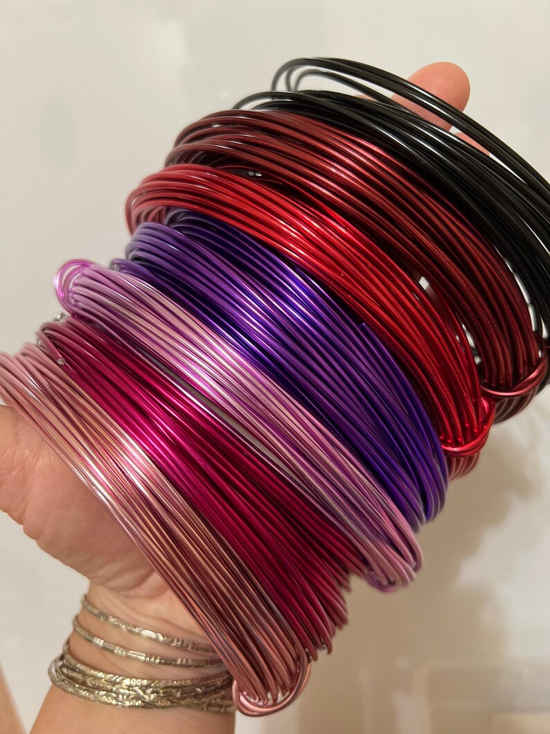May include: A stack of colorful aluminum wire in various shades of red, purple, and pink. The wire is coiled and ready for crafting projects.
