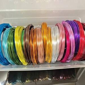 May include: A collection of 16 spools of colorful wire in a clear plastic container. The wire is arranged in a rainbow pattern, with each spool a different color.