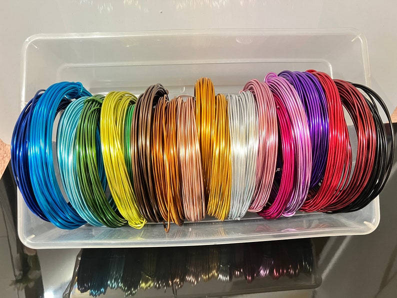 May include: A collection of 16 spools of colorful wire in a clear plastic container. The wire is arranged in a rainbow pattern, with each spool a different color.