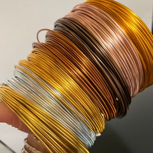 May include: A stack of different colored metal wires, including gold, silver, copper, and rose gold. The wires are arranged in a spiral pattern.