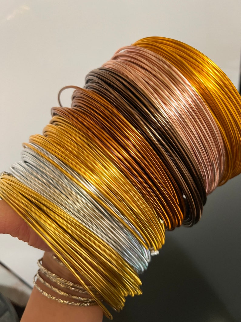 May include: A stack of different colored metal wires, including gold, silver, copper, and rose gold. The wires are arranged in a spiral pattern.