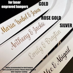 May include: Five white wooden hangers with laser engraved names in gold, rose gold, and silver metallic finishes. The text on the hangers reads "Maria Isabel & Jesus", "Anthony & Jackie", "Emily & Brayten", and "Alec & Abigail".