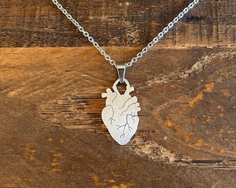 May include: A silver necklace with a detailed anatomical heart pendant.