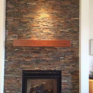 May include: A fireplace with a stone surround in a warm brown color called "Cinnamon". The fireplace has a wooden mantel and a black metal firebox with a glass door. The firebox is lit and has logs burning inside.