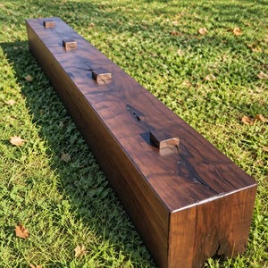 May include: A long, rectangular wooden beam with a dark walnut finish and black glaze. The top surface features four small, square wooden pegs spaced evenly along the length, with visible natural wood grain and dark cracks.