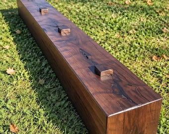 May include: A long, rectangular wooden beam with a dark walnut finish and black glaze. The top surface features four small, square wooden pegs spaced evenly along the length, with visible natural wood grain and dark cracks.