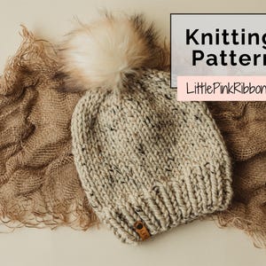 Puede incluir: Un gorro de punto grueso en color avena moteado con un gran pompón de piel sintética en la parte superior y una pequeña etiqueta de cuero marrón en el borde. La imagen incluye el texto Knitting Pattern y LittlePinkRibbons en una superposición.