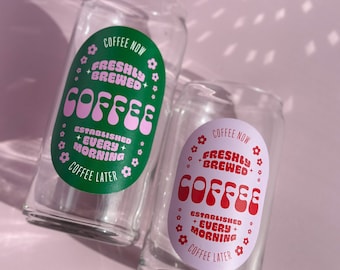 May include: Two clear glass cups with a pink and green design. The design says "Coffee Now Freshly Brewed Coffee Established Every Morning Coffee Later".