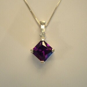 May include: A silver necklace with a square-shaped pendant featuring a large purple gemstone and smaller clear gemstones.