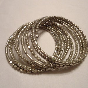 May include: A set of silver beaded bracelets, stacked and arranged in a circular pattern. The bracelets are made of small, round beads and are all the same size.