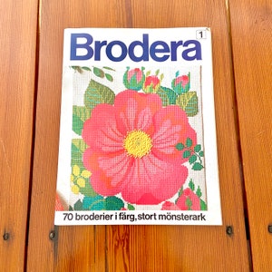 May include: A vintage embroidery magazine cover featuring a pink flower with yellow center and green leaves. The title "Brodera" is in blue text and the text "70 broderier i färg, stort mönsterark" is at the bottom.