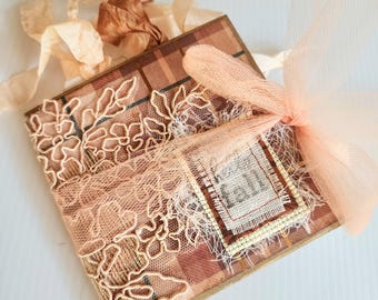 May include: A handmade, square-shaped journal with a plaid pattern in shades of brown and tan. The journal is adorned with delicate peach-colored lace and a matching tulle bow. A small tag reads "Fall".