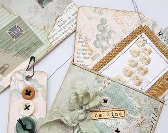 May include: A collection of handmade paper crafts, including envelopes, tags, and a small pouch. The items feature vintage-style floral patterns, buttons, lace, and ribbon. One tag has three buttons and the words "be kind" are visible on a small label.