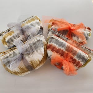 May include: Set of six small fabric pouches with zipper closures. The pouches are in two color patterns: brown and white, and orange and white. Each pouch is tied with a sheer ribbon.