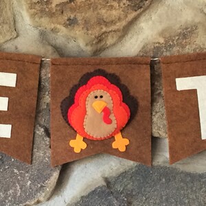 May include: A brown felt banner with the letters "E" and "T" in white felt. A felt turkey with orange, red, and brown feathers is in the center of the banner.