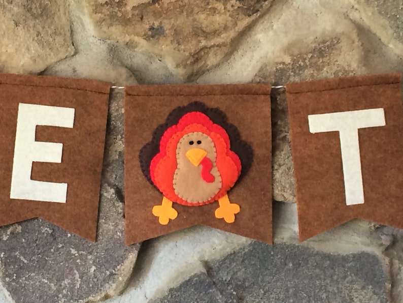 May include: A brown felt banner with the letters "E" and "T" in white felt. A felt turkey with orange, red, and brown feathers is in the center of the banner.