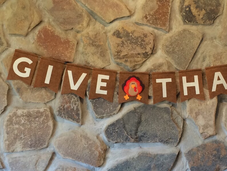 May include: A brown felt banner with white letters spelling "GIVE THANKS" and a brown felt turkey in the middle.